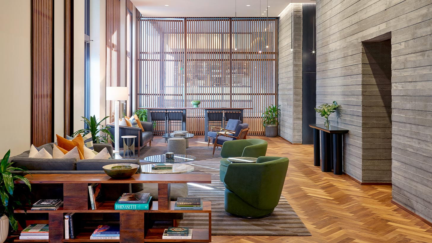 Limelight Denver's modern lobby features sofas, armchairs, coffee tables, wooden shelves with decor, large windows, and potted plants against textured walls.