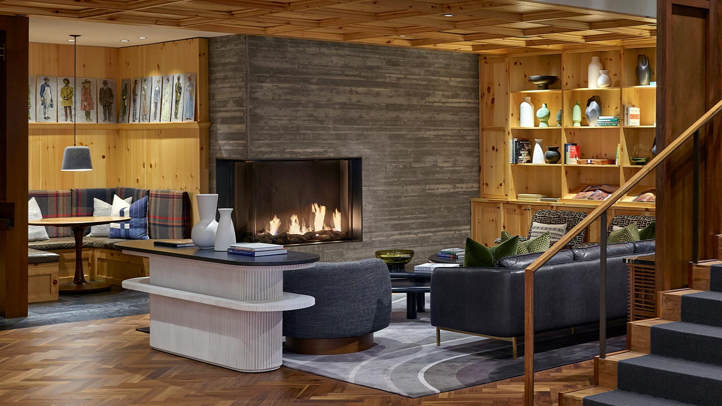 A stylish living area with a modern fireplace, wooden paneling, cozy seating nook, and bookshelves in a Limelight Denver room.