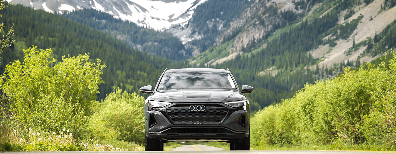 Audi cruises along flat road in Ketchum Idaho, green bushes around the car and tall snowy peaks in background