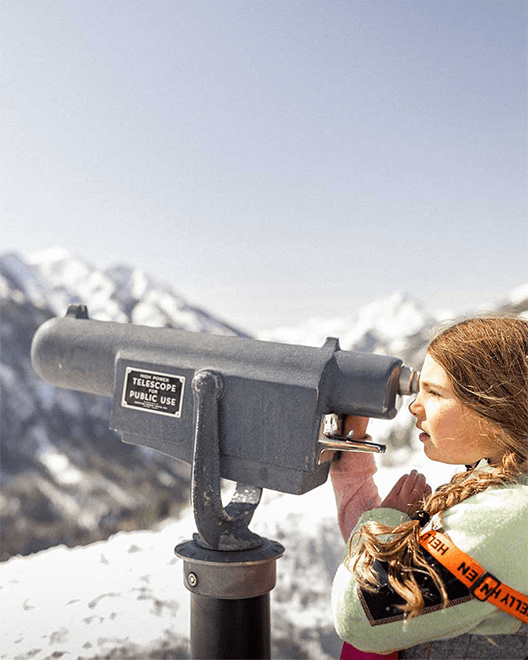 Little girl looks through binoculars at the mountain slopes at Snowmass