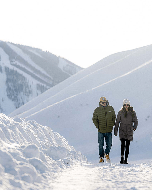 A couple walks hand in hand through tall snowdrifts at Limelight Ketchum