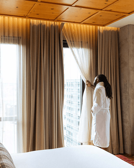 Man looks out of hotel curtains onto the city of Denver at his Limelight Hotel stay