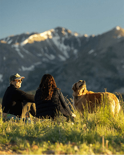 couple sits on ridge during sunset with their dog, during golden hour at Aspen Snowmass