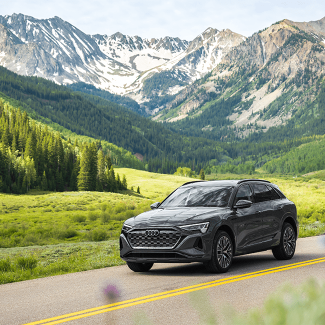 Audi drives along road in Snowmass, with summer mountain range in background